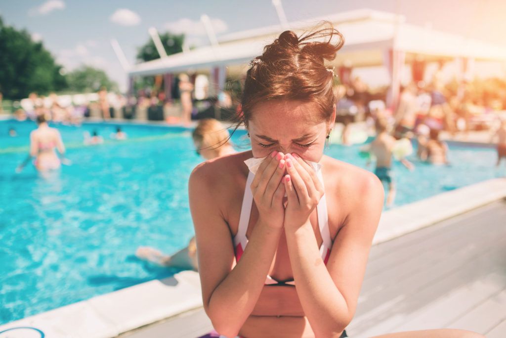 Kobieta w stroju kąpielowym, siedzi nad basenem z chusteczką przy nosie